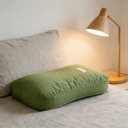 Light Green buckwheat pillow on a linen bed beside a lamp